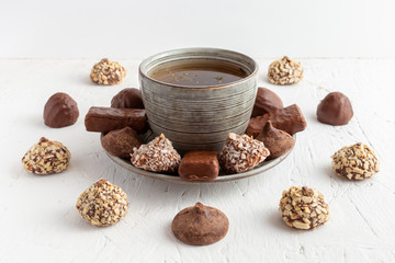 Tea with many chocolates. Tea cup with plate surrounded by an abundance of chocolate assortment carefully arranged.