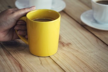 close up woman holding a yellow coffee cup on a wooden table in a coffee shop.
