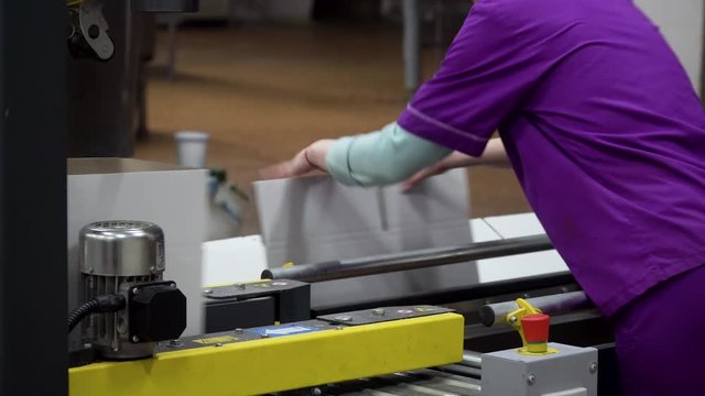 A factory worker lays out new boxes and puts them on a conveyor