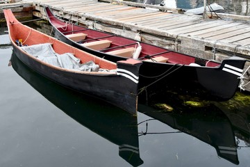 Two hand carved canoes are tied to a dock