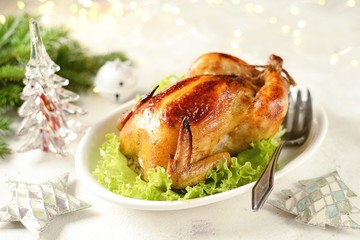 Roasted whole chicken on lettuce leaves. Christmas light background.