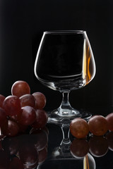 Cognac on the wall of a glass glass on a dark background with grapes