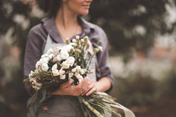 Young wman florist holding handmade bouquet with fresh flowers outdoors closeup.