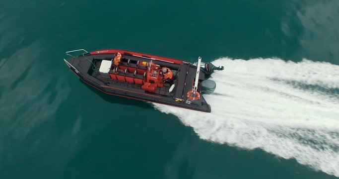The speedboat rushes over the Arctic ocean water somewhere near Spitsbergen. The white splashing trail stretches behind the boat. Beautiful view of red color of the boat on the turquoise water. Aerial