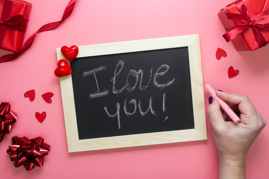 Valentine's day background. Female hands writting I lvoe you message on chalkboard frame, hearts and red ribbon, flat lay mock up with copy space. Love, 14 february.