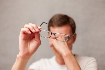 the young man holds glasses with diopter lenses and rubs his eyes from fatigue, fatigue of vision...