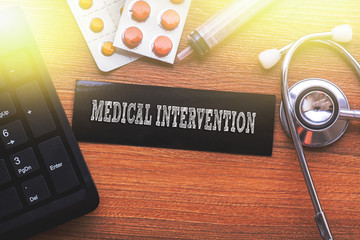 MEDICAL INTERVENTION words written on label tag with medicine,syringe,keyboard and stethoscope with...