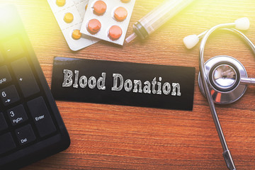 BLOOD DONATION words written on label tag with medicine,syringe,keyboard and stethoscope with wood background,Medical Concept