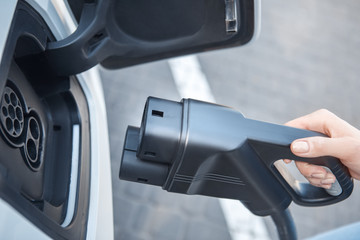 Transportation. Young woman on electric car having stop at charging station plugging charger top view close-up