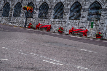 Red benches on the sidewalk along stone wall 