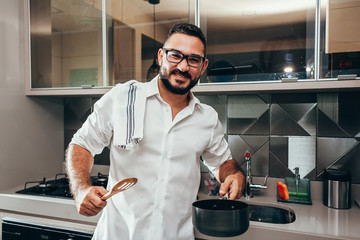 Young smiling man preparing meal in the kitchen of his home