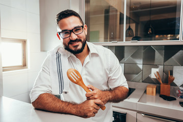 Young smiling man preparing meal in the kitchen of his home