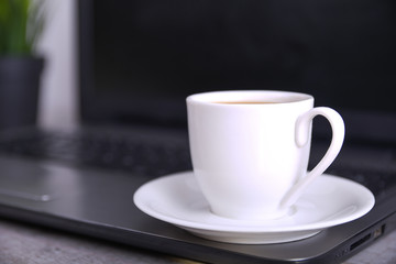  Cup of coffee on office desktop with laptop, computer on wooden table. Close up, with space for your text