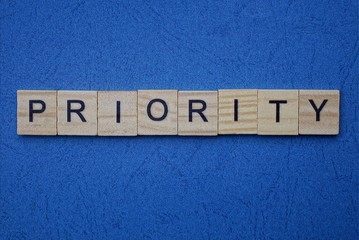 gray word priority from small wooden letters on a blue table