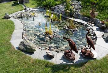 Zen ornamental pound, surrounded by metal bird sculptures. Embellished with rocks and the bottom...