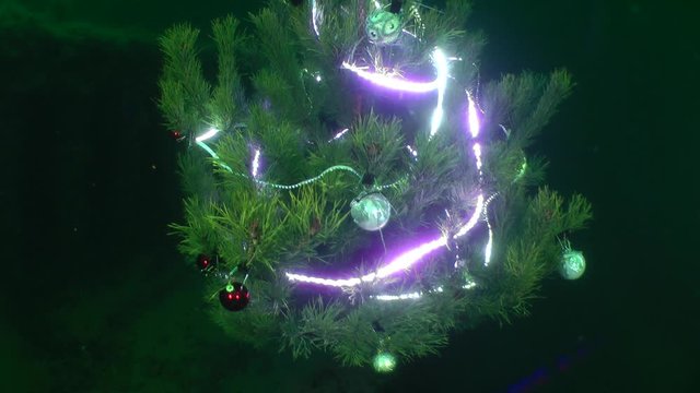 New Year celebration under water: Christmas tree with lit lights at the bottom of the sea, the camera moves from bottom to top.