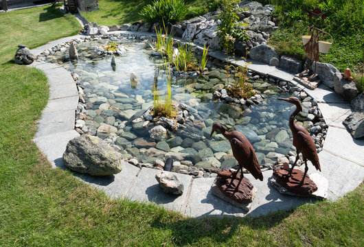 Zen ornamental pound, surrounded by metal bird sculptures. Embellished with rocks and the bottom lined with pretty stones. Water iris and aquatic plants.