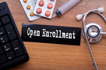 Open Enrollment words written on label tag with medicine,syringe,keyboard and stethoscope with wood...