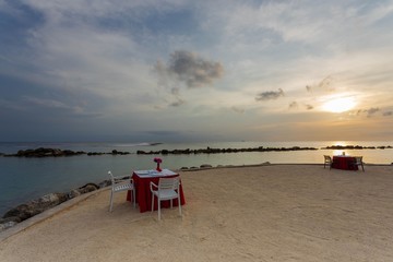 Gorgeous view of two romantic decorated tables on white sand beach on sunset. Turquoise water of...