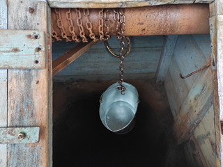 A metal bucket on an iron chain hangs in a well.