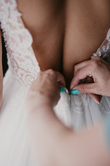 Women's hands mother corrects dress on the back of a bride with a beautiful embroidered veil and buttons. Close up hands. Morning bridal preparation details newlyweds. Wedding day moments, wear