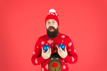 Winter decorations. How to handle top holiday stress triggers. New year concept. Hipster smiling cheerful bearded man wear winter sweater and hat hold balls. Christmas party. Winter holidays