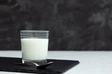 Bio kefir, Turkish ayran, milk or homemade yogurt in a glass glass are standing on a black stone board on a gray background next to a teaspoon of iron. Snack and source of pribiotics. Place for text.