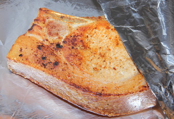 Baked piece of pork meat on aluminum foil, the process of cooking meat dishes in the oven.