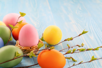 Multi-colored Easter eggs on a blue wooden table with twigs of birch with young leaves - Easter composition with copy space