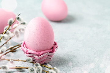 Pink Easter eggs in a wicker stand and on a gray table with pussy-willow twigs - Easter composition with copy space
