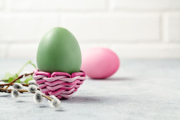 Pink and green Easter eggs in a wicker stand and on a gray table with pussy-willow twigs - Easter composition with copy space