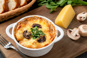 Casserole with chicken, mushrooms and cheese, known in Russia as julienne in white bowl with herbs on a wooden board, close up