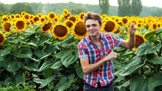 Successful male farmer dancing fun on sunflowers field, pleased and positive on sunset. Farming concept of bountiful harvest