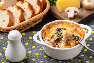 Casserole with chicken, mushrooms and cheese, known in Russia as julienne in white bowl with herbs on a kitchen towel
