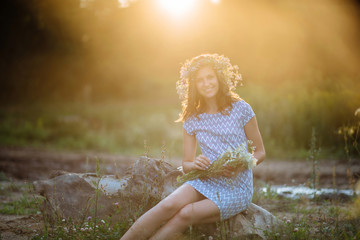 girl with flower wreath sitting in the field at sunset