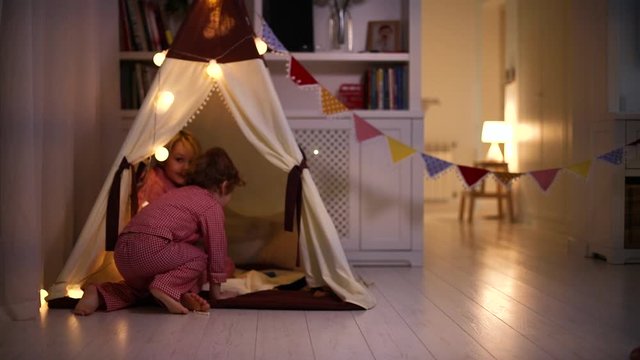 laughing kids, brothers having fun, running and playing in a teepee tent in the evening at home