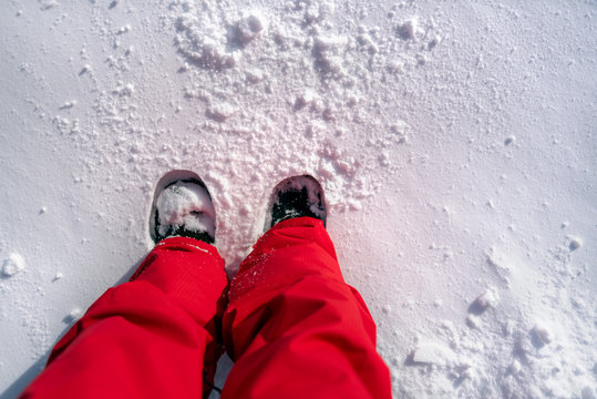 Person Wearing Red Ski Pants And Snow Boots Standing In The Snow.