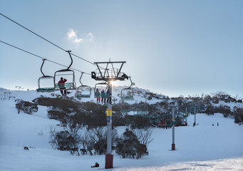 People riding a chairlift with a clear blue ski and the sun in the background at Smiggin Holes ski resort, Kosciuszko National Park, NSW Australia.