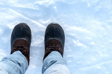 Person wearing blue jeans and snow boots standing in the snow.