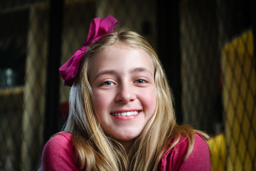 Portret of beautiful smiling blond hair girl with pink hair bow and pink sweater.