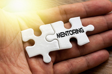 MENTORING written on White color of jigsaw puzzle with hand,conceptual