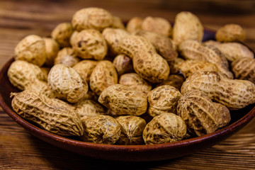 Ceramic plate with heap of unpeeled peanuts on wooden table
