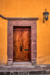 Fototapeta premium A freshly varnished brown door with a pink stone frame and an orange wall with a vintage wall lamp