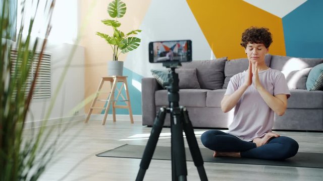 Yoga teacher is recoding video doing asanas meditating talking in modern apartment, vlogger is making content for internet vlog. Social media and youth concept.
