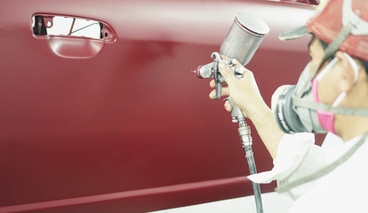 Car Repair auto mechanic worker painting a car in with airbrush pulverizer painting car body in paint chamber