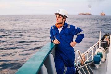 Marine Deck Officer or Chief mate seaman on deck of offshore vessel or ship , wearing PPE personal protective equipment - helmet, coverall looks at sea. ocean view