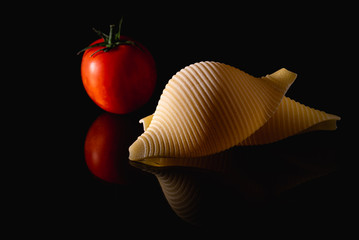Pasta Conchiglioni mit einer Tomate und Spiegelung auf einer glasplatte