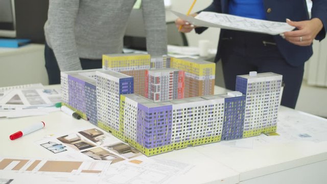Engineer with scheme in hand shows models of houses and explain something to workmate