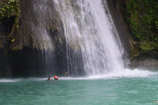 People swimming at tropical Kawasan falls and taking photos. People swimming under a powerful waterfall. 