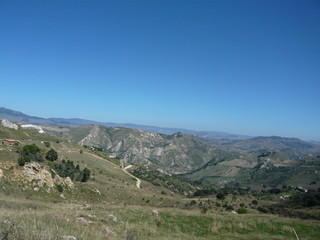 Fototapeta na wymiar Winding road to Enna, Sicily - Panorama of hills, outcroppings, mountains, house, sunshine everywhere, blue sky 